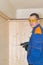 A worker in a blue uniform and yellow glasses holds a screwdriver in his hand for attaching a wooden bar to the ceiling