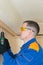 A worker in a blue uniform and yellow glasses screws a wooden block to the concrete ceiling with a screwdriver, close-up