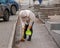 A worker with a broom sweeps the street from dust and debris. The janitor cleans the road. A female cleaner sweeps the sidewalk