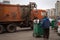 The worker carries a container with garbage to the garbage collection machine during garbage collection on the street.