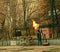 A worker cleans old paint from a metal fence using fire. A man holds a gas burner with a lit flame