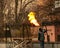 A worker cleans old paint from a metal fence using fire. A man holds a gas burner with a lit flame