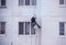 A worker climber paints a residential high-rise building and seals up joints in a house, painting a residential house, close-up