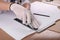 Worker cutting paper with utility knife and ruler at wooden table, closeup