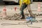 Worker drilling concrete driveway with jackhammer.