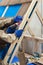 Worker with electric drill installing brown roof metal tile on wooden house.