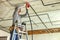 Worker electrician standing on aluminium ladder installing electrical cables laid in protective corrugation installed on the