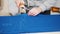 Worker at the factory cutting blue cloth using special instrument following the marks. Close up