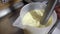 Worker at food factory preparing ice cream using a professional blender in a bucket mixing cold cream with freshly squeezed orange