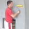 a worker glues wallpaper on the wall with a fireplace using a rubber roller.