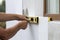 Worker hand with level and knife measuring and cutting white rigid polyurethane foam sheet on wall at newly installed plastic wind