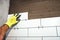Worker holding ceramic tiles and applying cement adhesive on bathroom walls