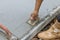 This worker is holding a steel trowel and smoothing out the plastering of a new sidewalk on a freshly laid concrete slab