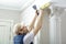 Worker holds putty knife and measures the wall corner using metal angle.