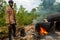 Worker igniting charcoal barrels for road construction. Intense flames and billowing black smoke from tar burning. Construction in