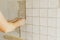 Worker installing stylish white tiles on plaster wall in sunlight. Hands laying modern square tile on adhesive close up. Kitchen