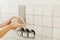 Worker installing stylish white tiles on wall at electricity socket. Hands laying modern square tile on adhesive close up.