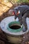 A worker installs a sewer manhole on a septic tank made of concrete rings. Construction of sewage disposal systems for