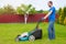 Worker with a lawn mower mows grass in the garden. Side view