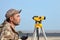 Worker with level, surveyor builder with geodesy equipment close to highway, with mobile phone, smiling.