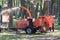 Worker looking upward in a woodland area with working wood chipping machine