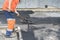 Worker man lays asphalt road repair road paving yellow sun ray light. A man in overalls is laying asphalt with a shovel