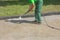 Worker man in uniform washes street or park sidewalk. Municipal service of city cleaning process. Guy uses water spray equipment