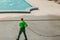 Worker man in uniform washes street or park sidewalk near water pool or fountain. Municipal service of city cleaning process. Guy