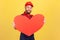 Worker man wearing overalls and red cap holding big red heart, fast gifts delivery during holidays.