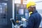 Worker man with yellow helmet and ear protection typing keyboard of laptop computer at factory