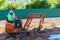 A worker on a minitractor rakes the earth with a bucket. Land works.