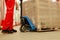 Worker moving wrapped wooden pallets with manual forklift in warehouse, closeup