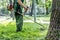 Worker mowing tall grass with electric or petrol lawn trimmer in city park or backyard. Gardening care tools and