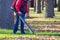 Worker operating heavy duty leaf blower in city park. Removing fallen leaves in autumn. Park cleaning service