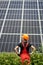 Worker in orange uniform stands with his back to camera against the background of large plantation solar batteries