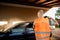 A worker in an orange vest washes the car. A man spraying pressure washer for car wash in car care shop. Back view