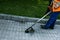 A worker in overalls with a trimer in his hands mows the grass on the lawn and paths in the park.