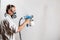 Worker painting wall with spray gun in white color.