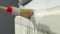 A worker paints a heating radiator with a brush.