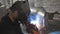 Worker in protective mask welding metal construction at metalworking factory. Welder doing joint between two steel