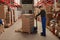 Worker pulling manual pallet truck with boxes wrapped in stretch film at warehouse