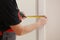 Worker in red cap and work suit with the measuring tape. Man is installing the doors. Measure tape in hands. Repair