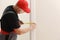 Worker in red cap and work suit with the measuring tape. Man is installing the doors. Measure tape in hands. Repair works.