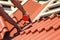 Worker on a roof with electric drill installing red metal tile on wooden house.