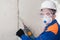 Worker in safety glasses, helmet and mask drills a wall with a hammer drill, looks at the camera