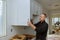 Worker sets a new handle on the white cabinet with a screwdriver installing kitchen cabinets