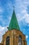 Worker without shirt hanging from a harness on a steep copper roof and doing repair work on an old church steeple against a