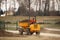 A worker on a small orange dump truck is transporting and emptying the ground forming the landscape at a sports stadium.