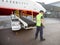 Worker Standing By Luggage Conveyor Attached To Airplane