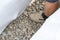 A worker stands in a drainage trench with white geotextile. Feet of the craftsman on the granite rubble closeup.